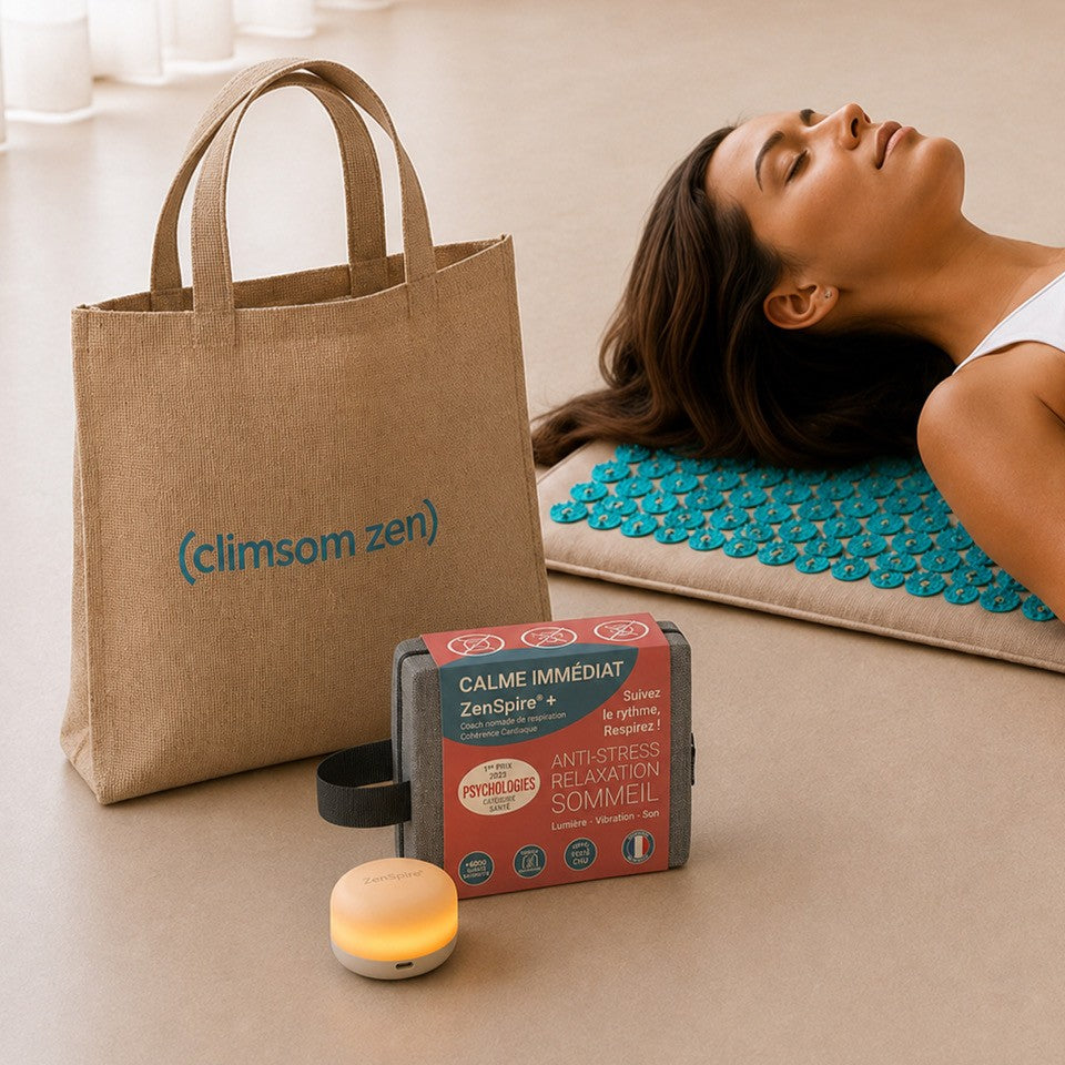Le sac de transport Climsom Zen, la boîte du ZenSpire + et le ZenSpire + allumé, devant une femme allongée sur le tapis d’acupression